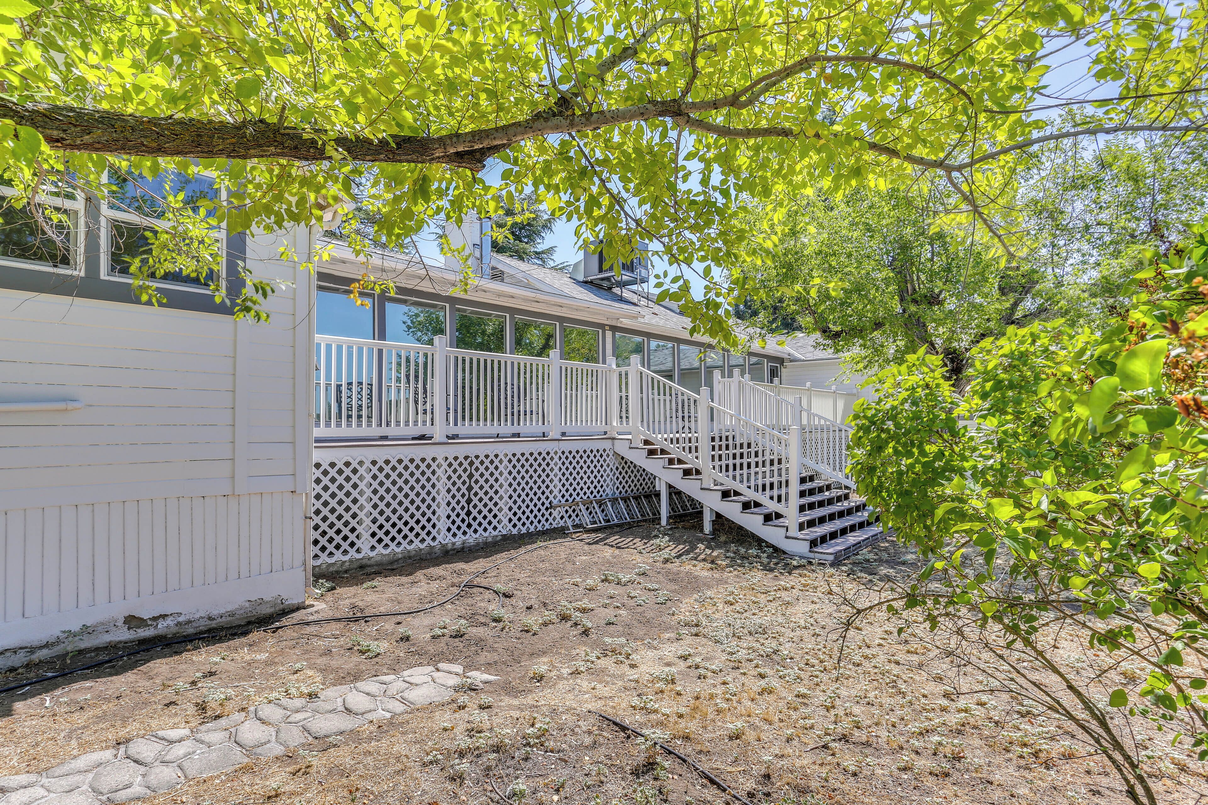 A covered outdoor area with a white fence, a staircase, and a view of a house in the background.