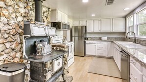 A kitchen with a stone wall, white cabinets, stainless steel appliances, and a built-in wood stove. - Spacious Coarsegold Getaway ~ 34 Mi to Yosemite! (Coarsegold)