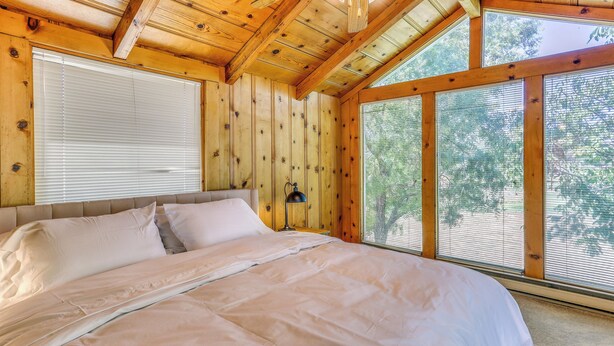 A wooden cabin bedroom with a large bed, a ceiling fan, and large windows. - Spacious Coarsegold Getaway ~ 34 Mi to Yosemite! (Coarsegold)