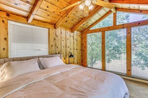 Un dormitorio de cabaña de madera con una cama grande, un ventilador de techo y ventanas amplias.