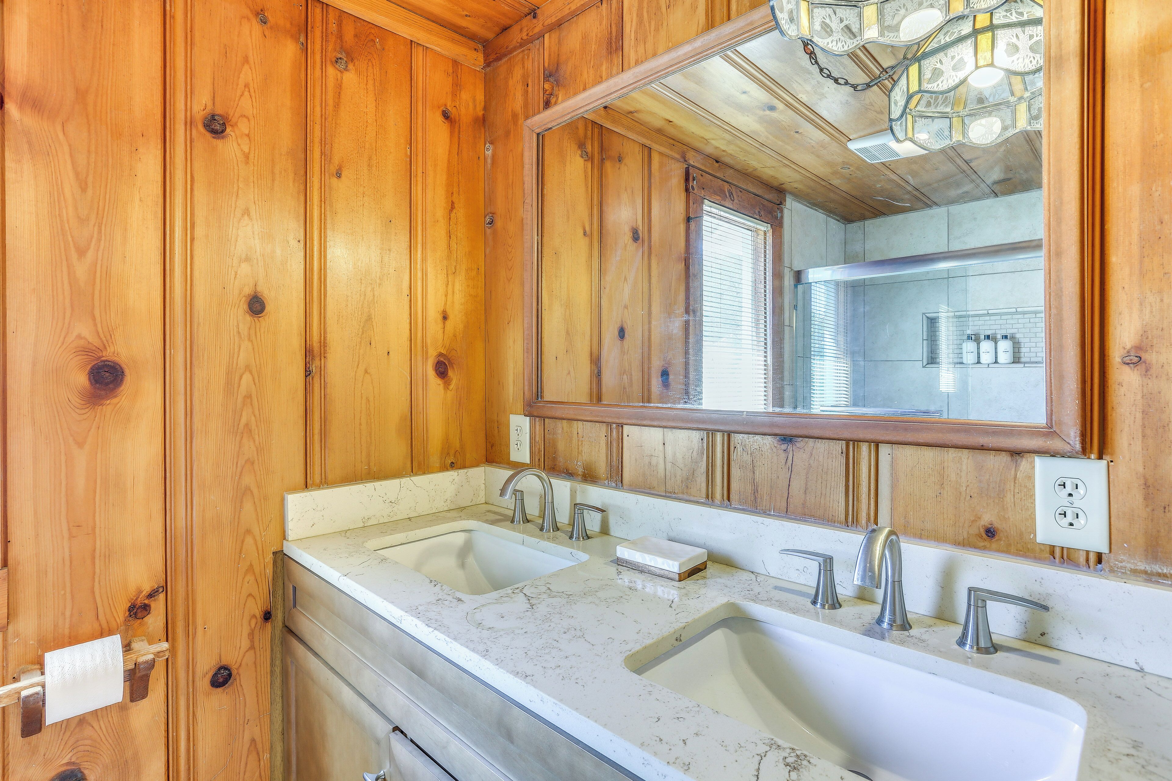 A wooden cabin bathroom with two sinks, a large mirror, and a chandelier.