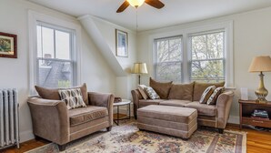 A living room with two sofas, a patterned rug, and a ceiling fan. - Charming Victorian 1BR Near Hospitals & Downtown (Providence)