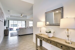 A modern living room with a wooden floor, a sofa, a console table with lamps, and a large mirror.