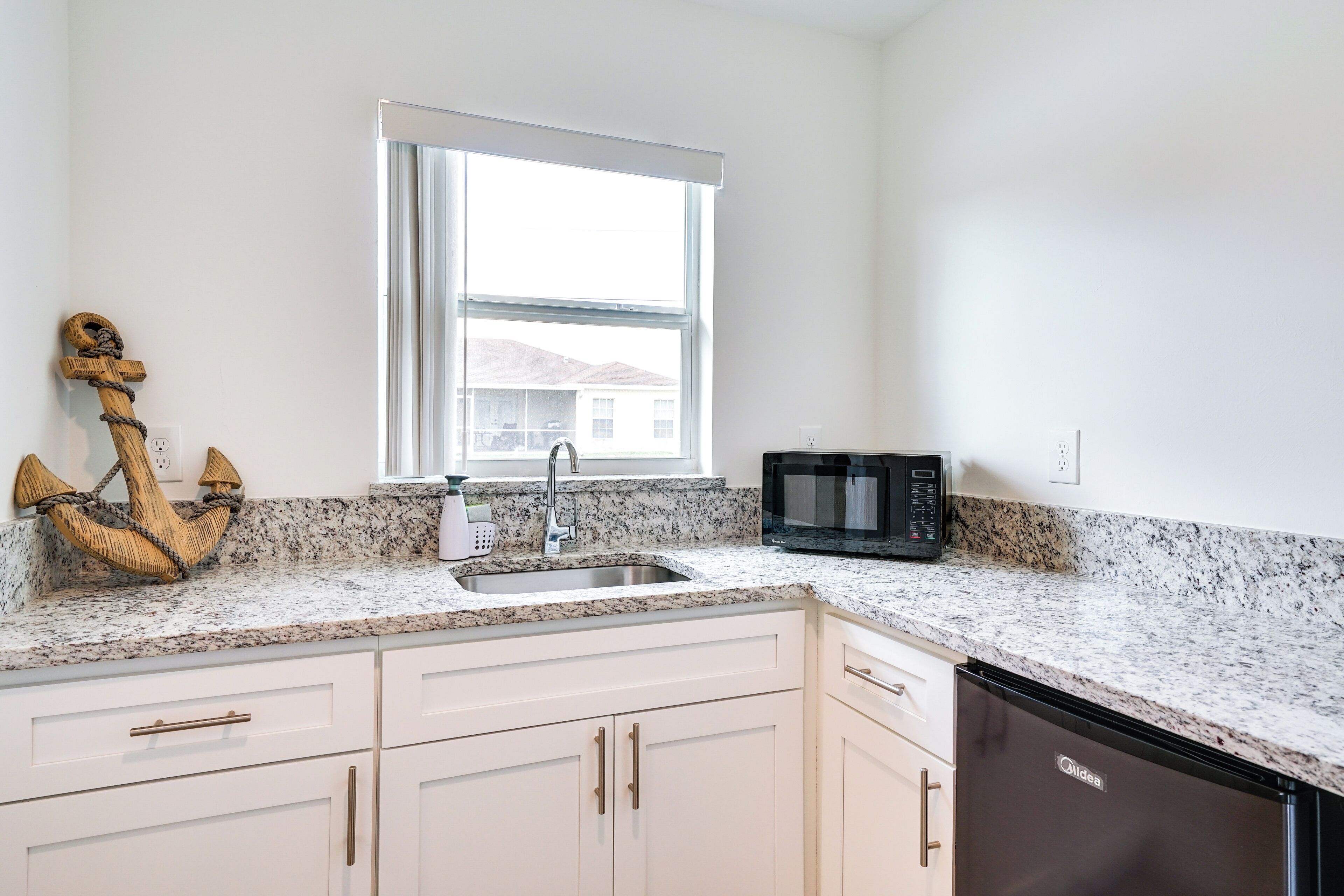 A kitchen with white cabinets, a granite countertop, a sink, a microwave, and a dishwasher.
