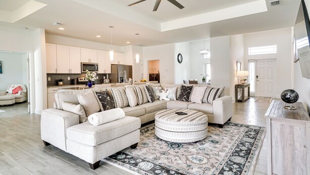 A spacious living room with a large sectional sofa, a round ottoman, and a patterned rug. - Furnished Lanai & Yard: Comfy Lehigh Acres Getaway (Lehigh Acres)