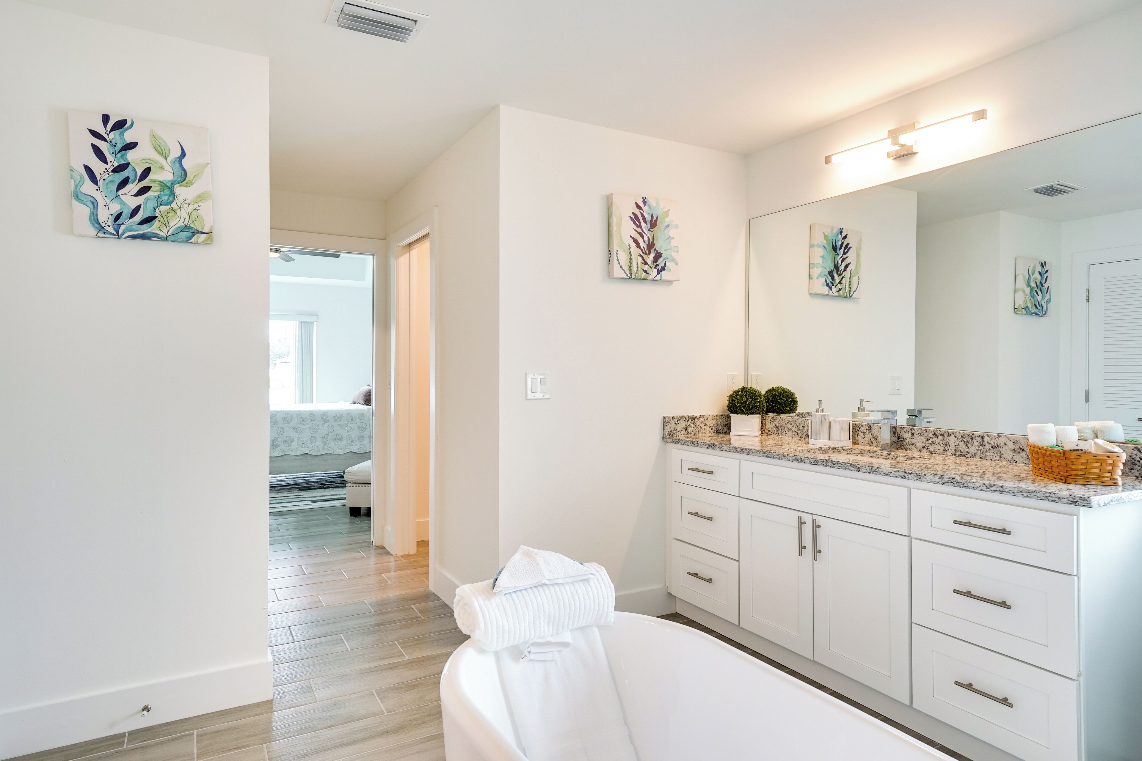 A modern bathroom with a large mirror, white cabinetry, and artwork on the walls.
