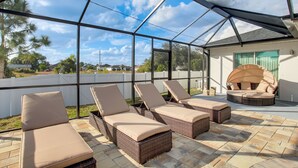 A covered outdoor patio with wicker lounge chairs and a round seating area. - Furnished Lanai & Yard: Comfy Lehigh Acres Getaway (Lehigh Acres)