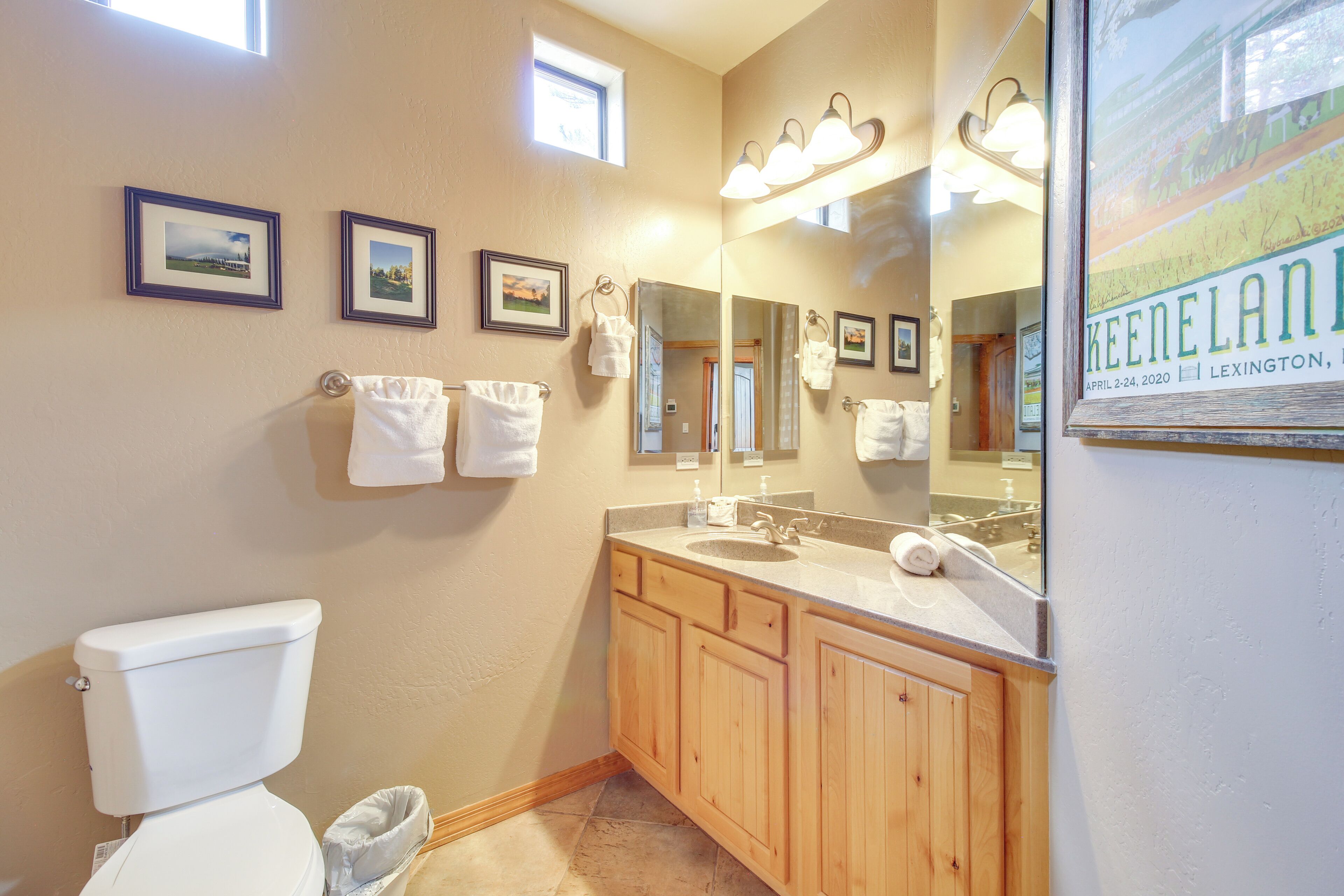 A bathroom with a toilet, sink, wooden cabinets, and framed pictures on the wall.