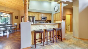 Une cuisine spacieuse avec des meubles de rangement en bois, un îlot central doté de tabourets et une horloge au mur.