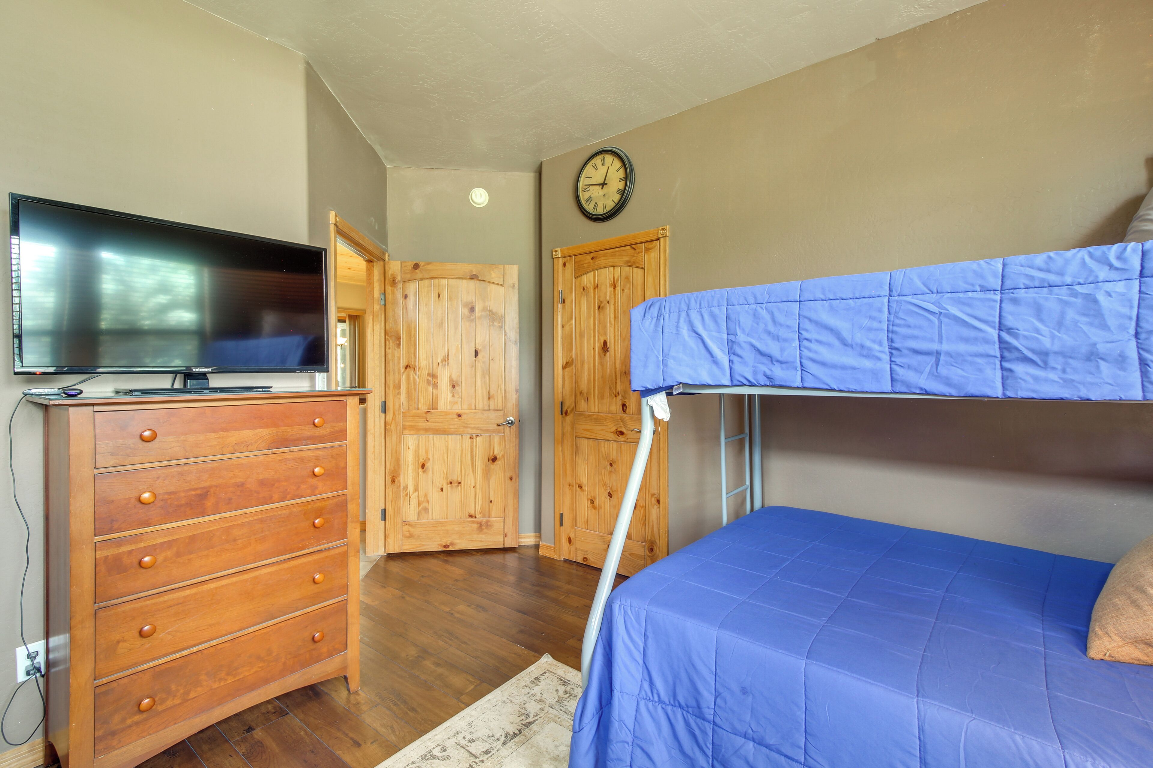 A bedroom with a bunk bed, wooden dresser, television, and a clock on the wall.