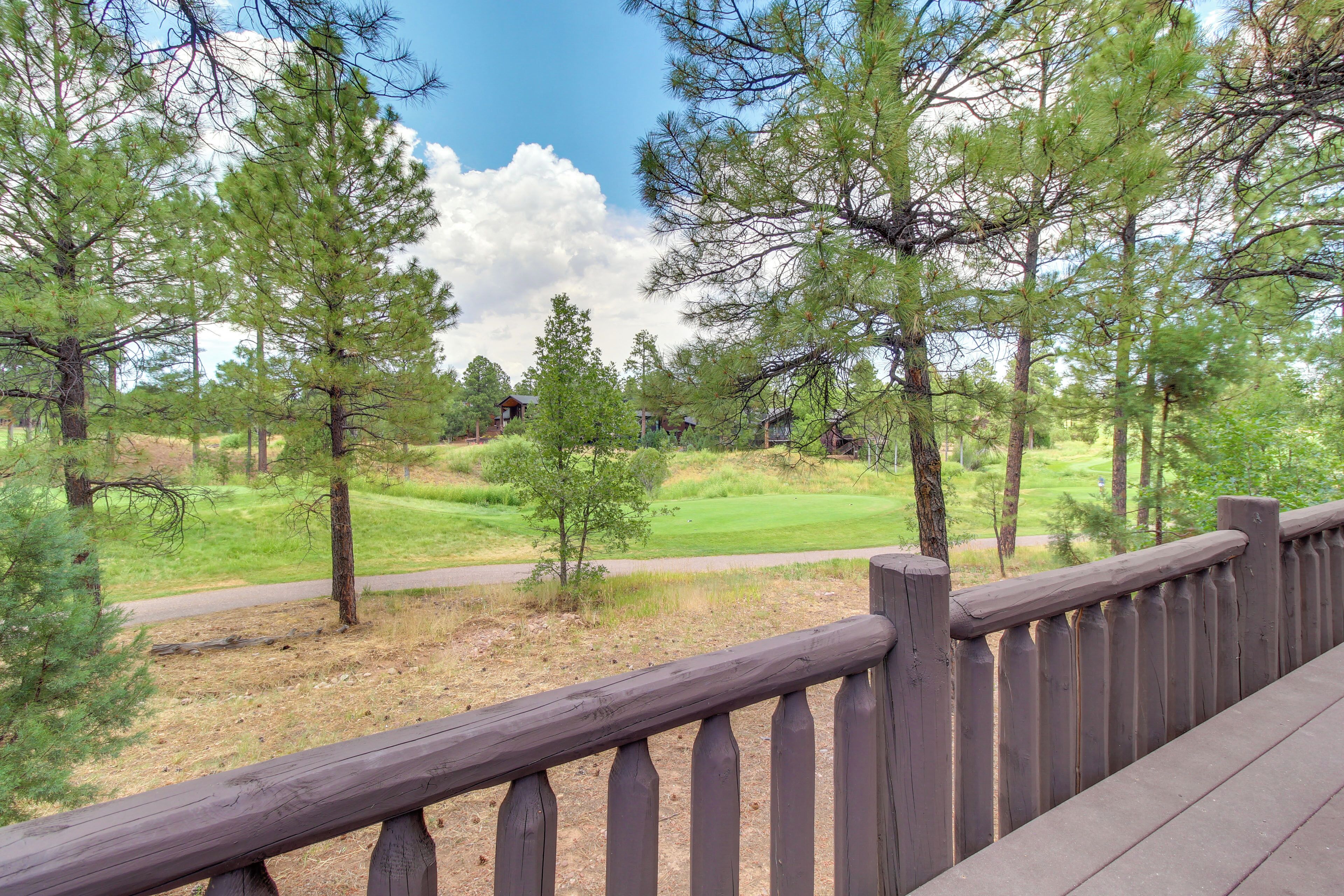 A wooden deck overlooking a golf course with pine trees and a clear sky.