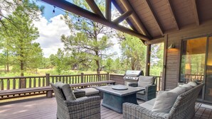 Une terrasse extérieure couverte, aménagée avec des meubles en osier, un barbecue et offrant une vue sur les arbres environnants.