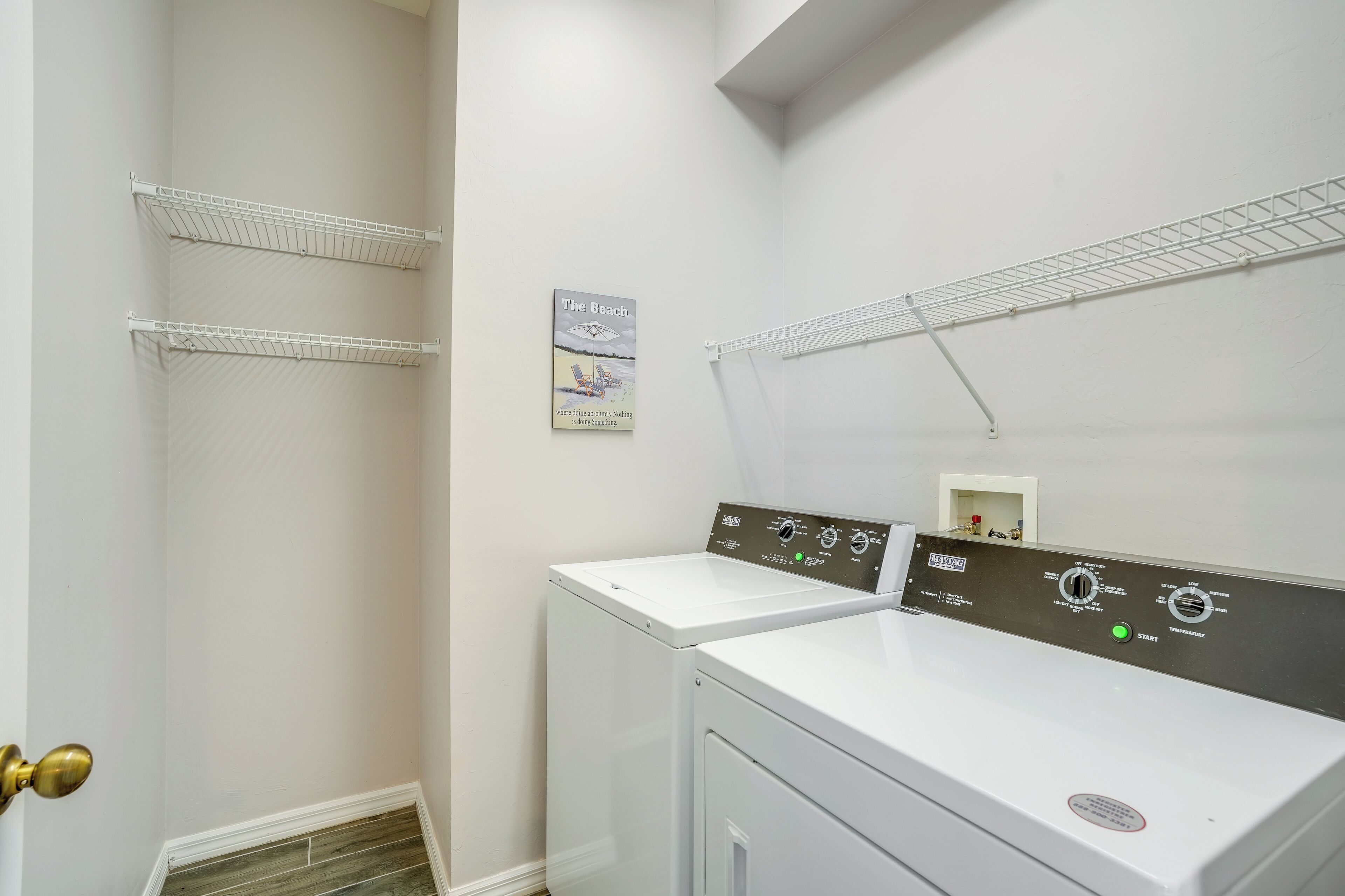 A laundry room with two white washing machines, metal drying racks, and a wall-mounted thermostat.