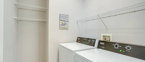 A laundry room with two white washing machines, metal drying racks, and a wall-mounted thermostat.