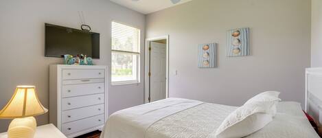 A bedroom with a bed, a dresser, a lamp, a ceiling fan, a TV, and a window.