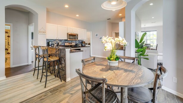 A modern kitchen with white cabinets, a central island, and a dining area with a round table and chairs. - Sunny Fort Myers Home w/ Heated Pool! (Fort Myers)