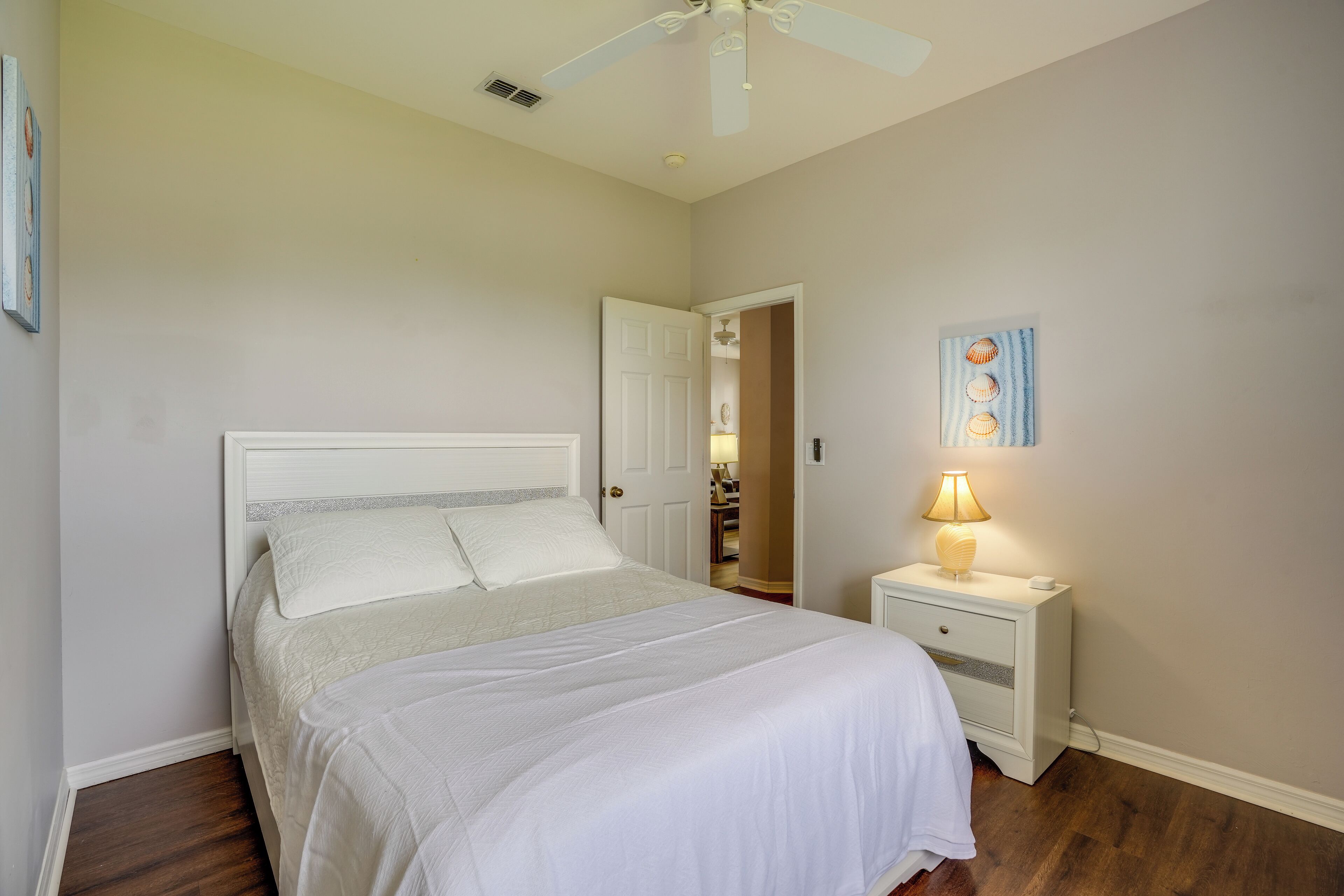 A bedroom with a bed, a nightstand with a lamp, a ceiling fan, and a door leading to a bathroom.