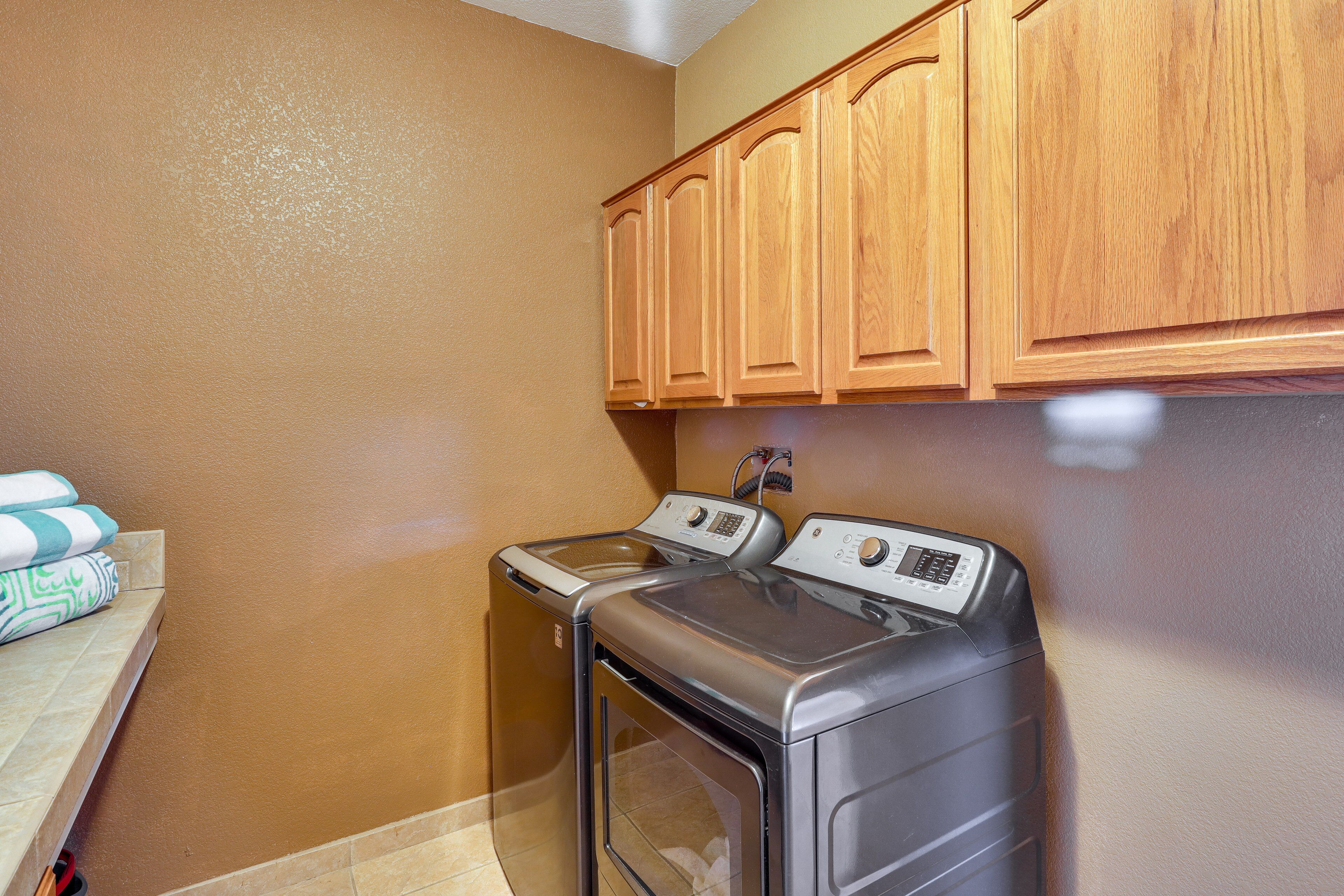 A laundry room with two washing machines, wooden cabinets, and a tiled floor.