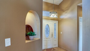 Un couloir avec une porte blanche, une plante en pot et un tapis à motifs.