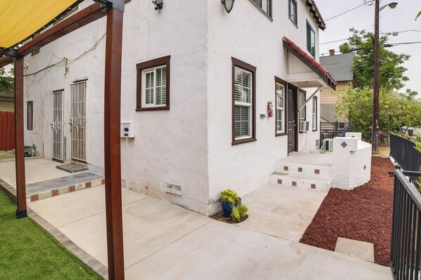 A white building with brown trim, a covered porch, and a small garden area with mulch and a potted plant. - Pet-friendly Riverside Vacation Rental w/ Patio! (Riverside)