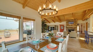 Un coin repas avec une table en bois dressée pour six personnes, un lustre et une vue sur l’extérieur.
