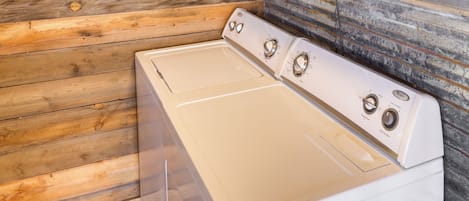 A white washer and dryer in a corner with wooden walls and a stone accent wall.