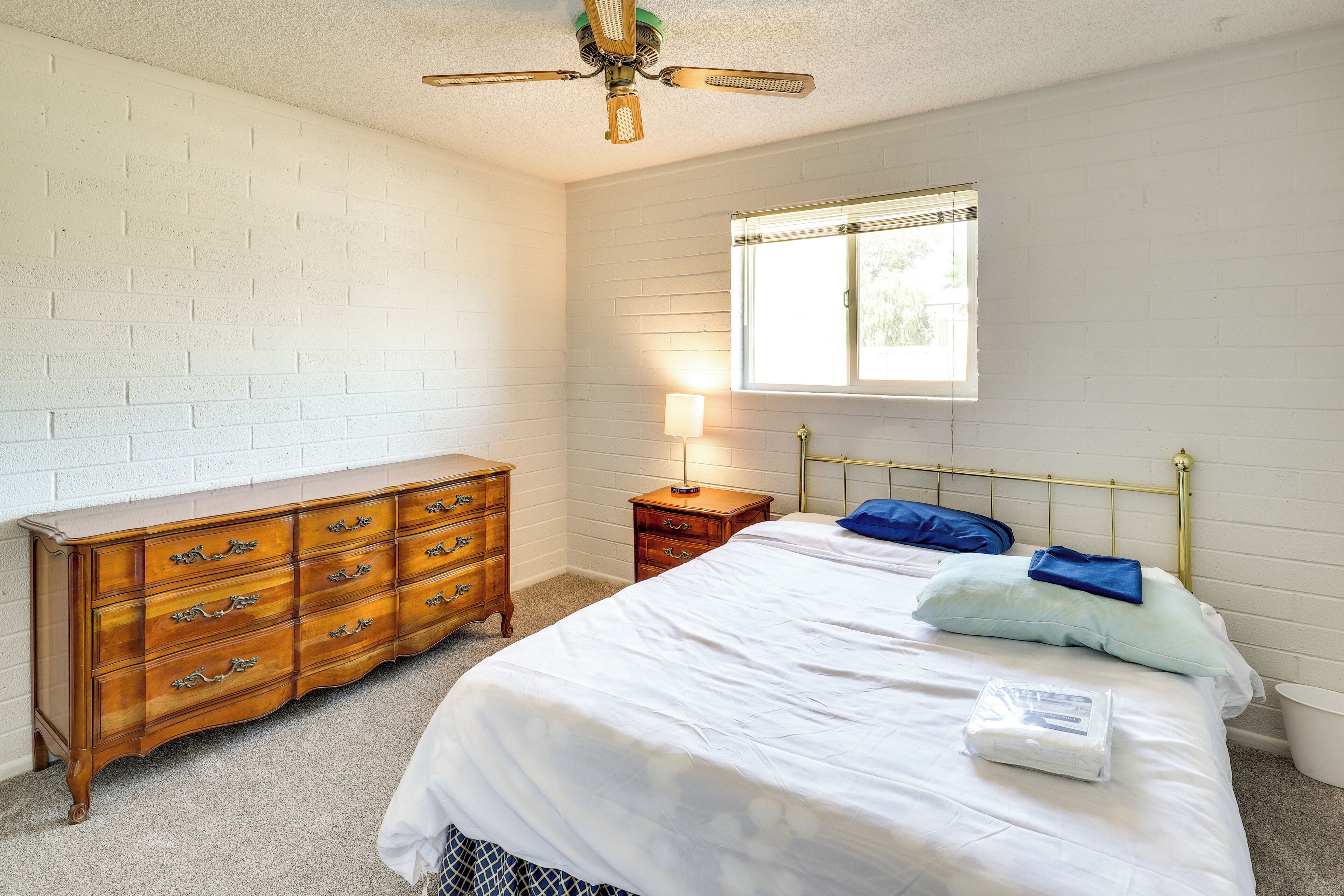 A bedroom with a bed, dresser, nightstand, lamp, and window.