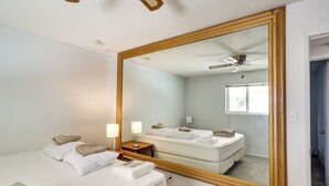 A hotel room with a large mirror, a bed with white linens, a bedside table with a lamp, and a ceiling fan. - Riverfront Bullhead City Home w/ Mountain Views! (Bullhead City)