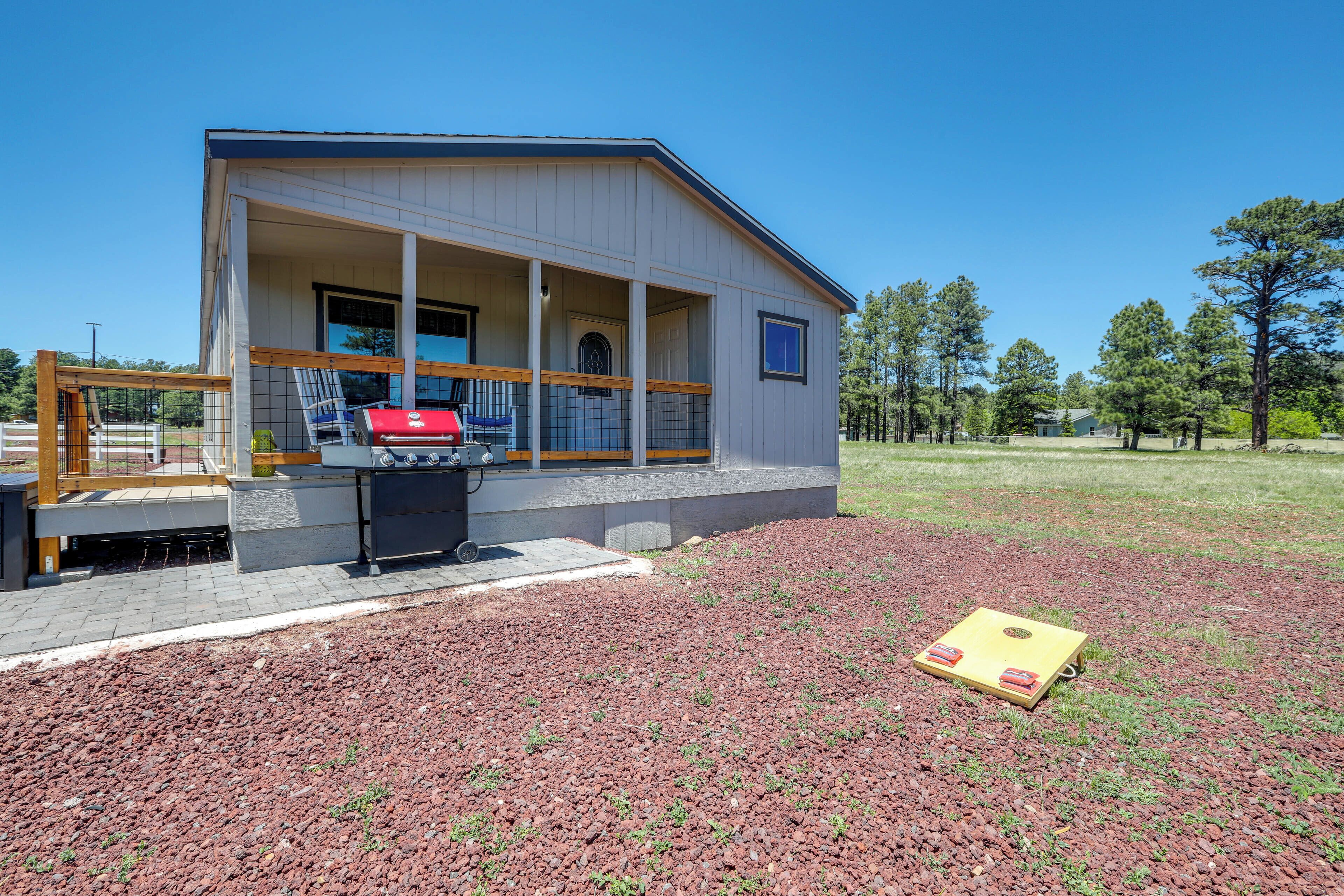 A modern house with a covered porch, a barbecue grill, and a yard with a red gravel surface.