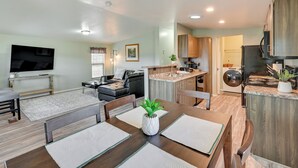 Un espacio de sala y comedor moderno y abierto, con cocina, televisor de pantalla plana y mesa de comedor con individuales.