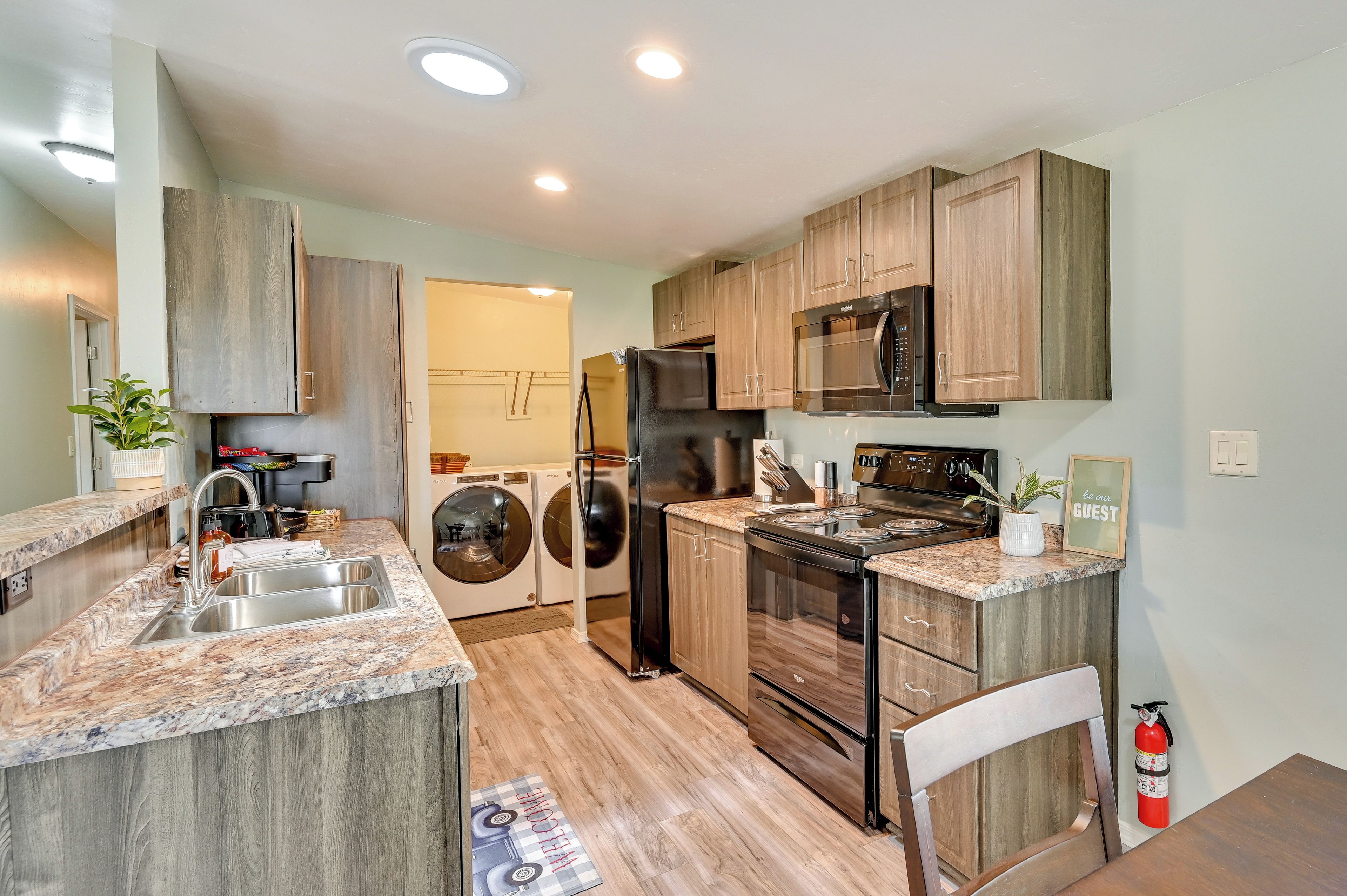 A modern kitchen with granite countertops, wooden cabinets, a stainless steel refrigerator, a microwave, and a stove.