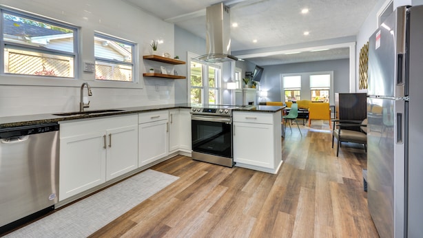 Une cuisine moderne avec des armoires blanches, des appareils en acier inoxydable et un plancher en bois.