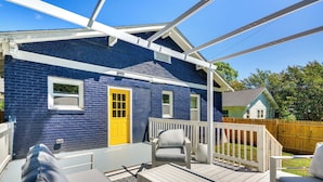 Une maison bleue avec une porte jaune, des meubles de véranda blancs et une terrasse en bois.