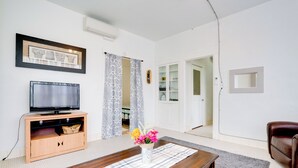 A living room with a wooden entertainment unit, a flat-screen TV, a coffee table with a vase of flowers, and a brown leather sofa. - Downtown Schertz Vacation Rental Near Restaurants! (Schertz)