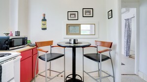 A compact kitchen with a microwave, stove, and red cabinets. There is a small round table with two chairs and a framed picture above it. - Downtown Schertz Vacation Rental Near Restaurants! (Schertz)