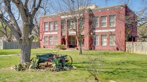 A red brick two-story house with a front porch, a tree in the yard, and a green cart. - Downtown Schertz Vacation Rental Near Restaurants! (Schertz)