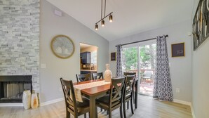 Un coin repas avec une table et des chaises en bois, une cheminée et une vue sur une terrasse extérieure, accessible par une porte vitrée.