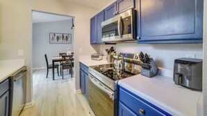 Une cuisine moderne avec des meubles bleus, des appareils en acier inoxydable et un coin repas comprenant une table et des chaises.