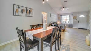 Un coin repas avec une table en bois, des chaises et un vase servant de centre de table. On y trouve également un ventilateur de plafond et une œuvre d’art encadrée accrochée au mur.