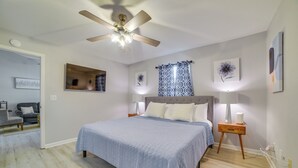Une chambre à coucher avec un lit, un ventilateur de plafond, une table de chevet avec une lampe et une fenêtre ornée de rideaux à motifs.
