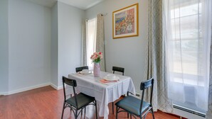 Un coin repas avec une table dressée pour quatre personnes, des chaises, un vase rempli de fleurs et un tableau accroché au mur.