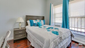 Une chambre à coucher avec un lit, une table de chevet, une lampe et une fenêtre avec des rideaux.