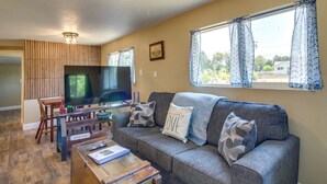 A cozy living room with a grey sofa, wooden coffee table, and a television. - On-site Creek & Fishing: Cozy Coos Bay Retreat! (Coos Bay)