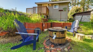 A rustic outdoor seating area with Adirondack chairs, a wooden barrel fire pit, and a wooden deck. - On-site Creek & Fishing: Cozy Coos Bay Retreat! (Coos Bay)