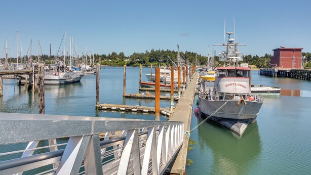 A marina with boats docked, a bridge, and a red building in the background. - On-site Creek & Fishing: Cozy Coos Bay Retreat! (Coos Bay)