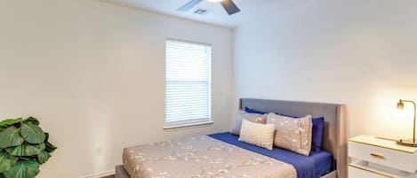A bedroom with a bed, a nightstand, a ceiling fan, a window with blinds, and a potted plant.