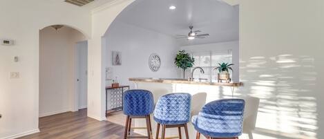 Une cuisine moderne dotée d’un coin bar, avec des tabourets de bar bleus, un ventilateur de plafond et une fenêtre avec des stores.