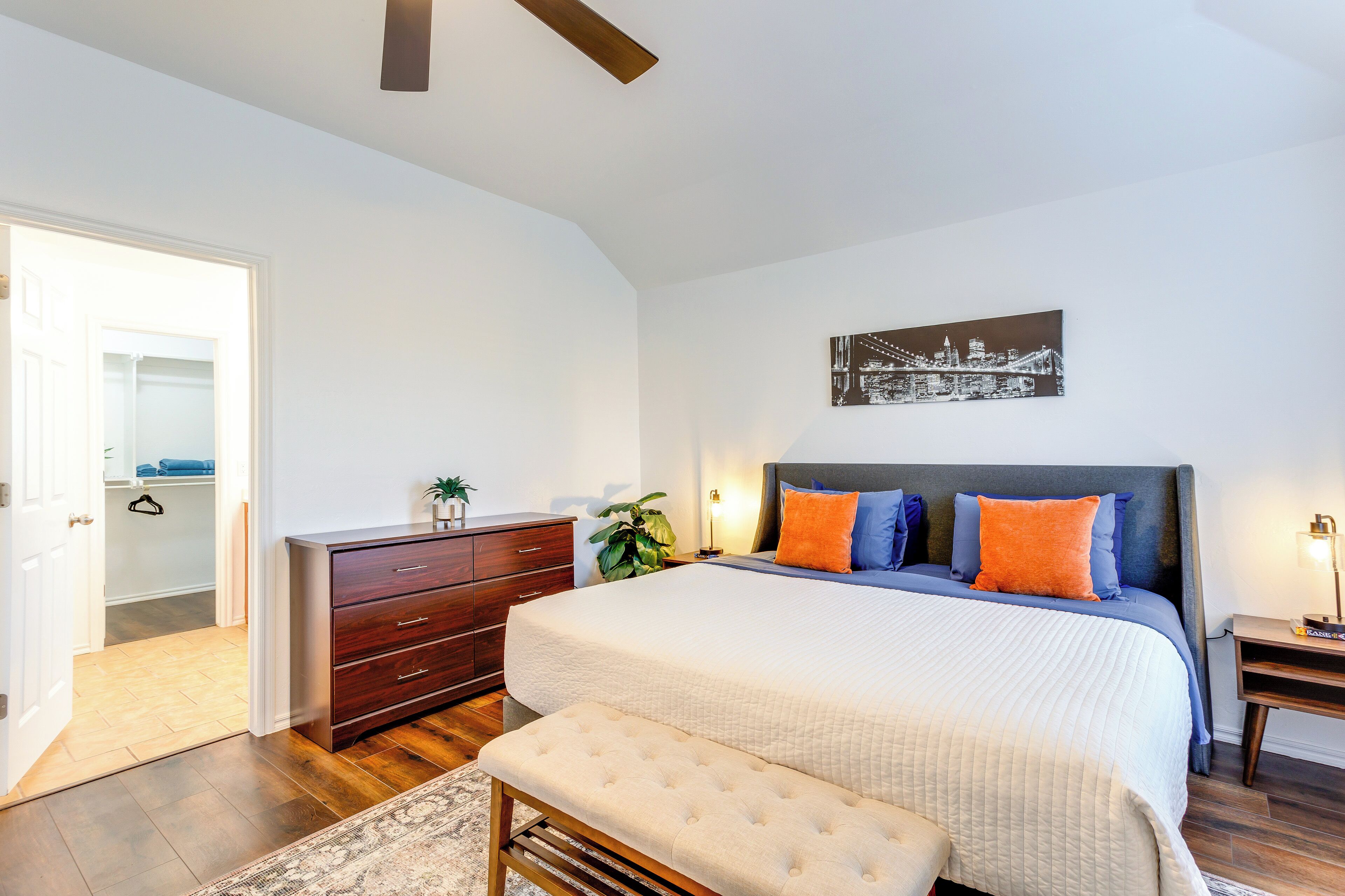 A bedroom with a large bed, a bench, a dresser, a closet, and a ceiling fan.