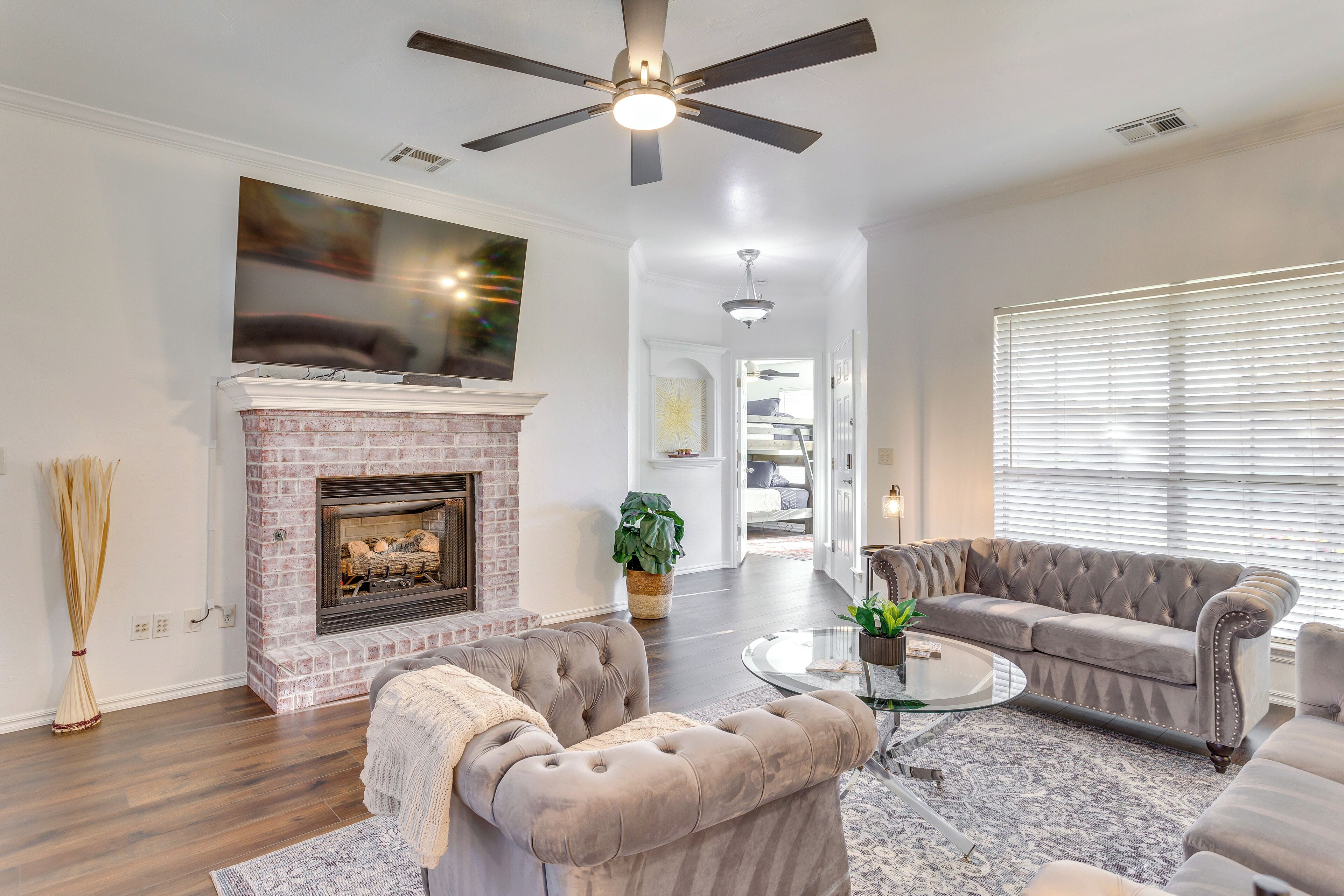 A living room with a fireplace, a ceiling fan, a large flat-screen TV, and a grey sofa.