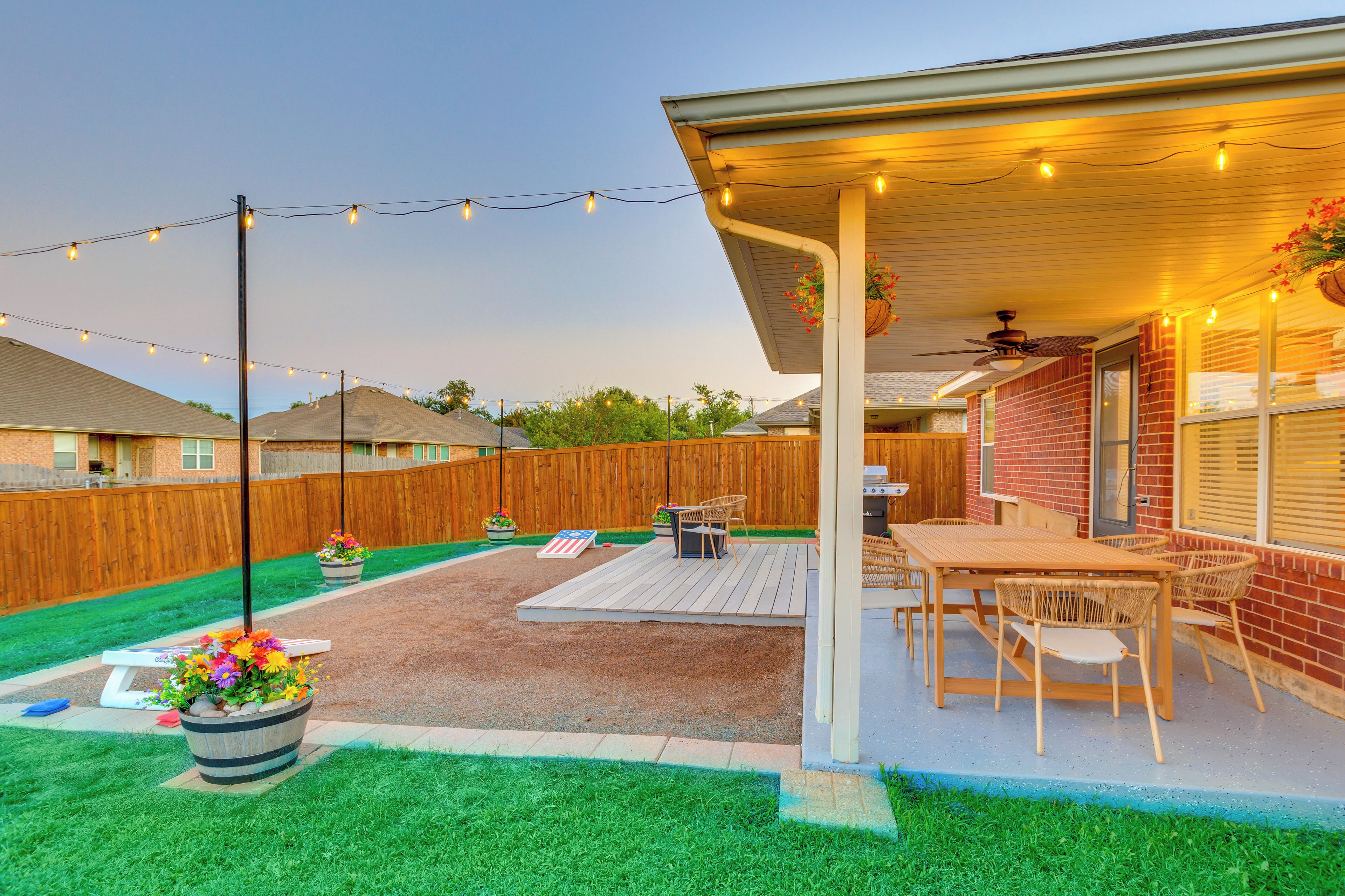A backyard patio with a wooden deck, outdoor furniture, and string lights.
